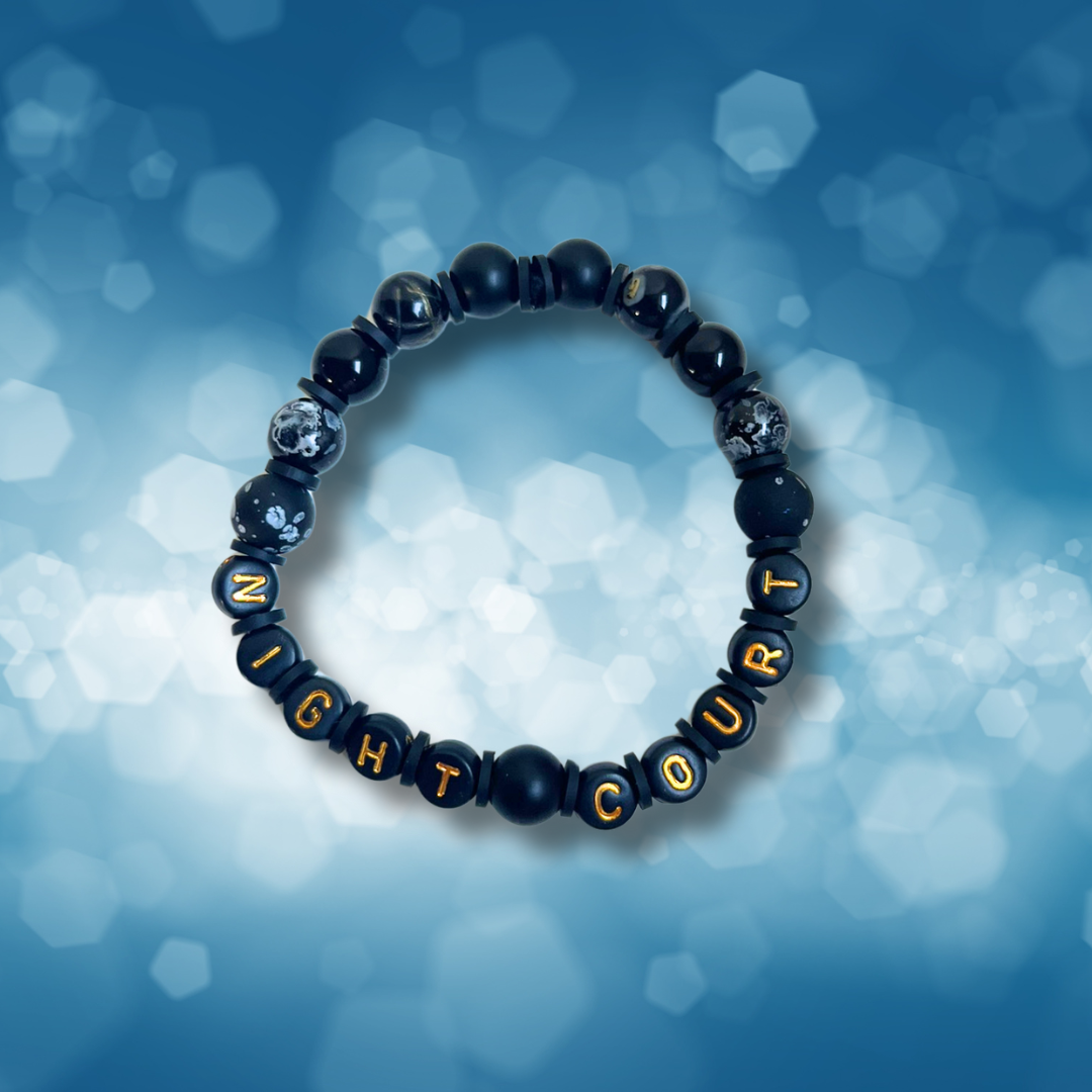 Black beaded bracelet with the words Night Court, on a blue background.