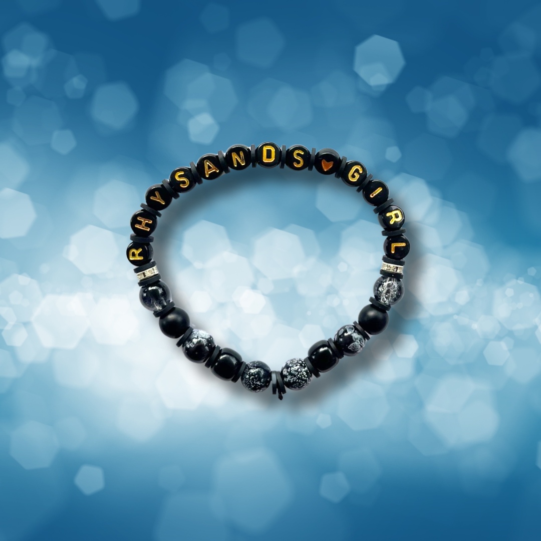 Black beaded bracelet with the words Rhysands Girl, on a blue background.