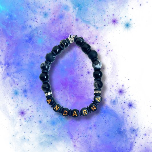Black beaded bracelet with the word Andarna, on a purple and blue background.