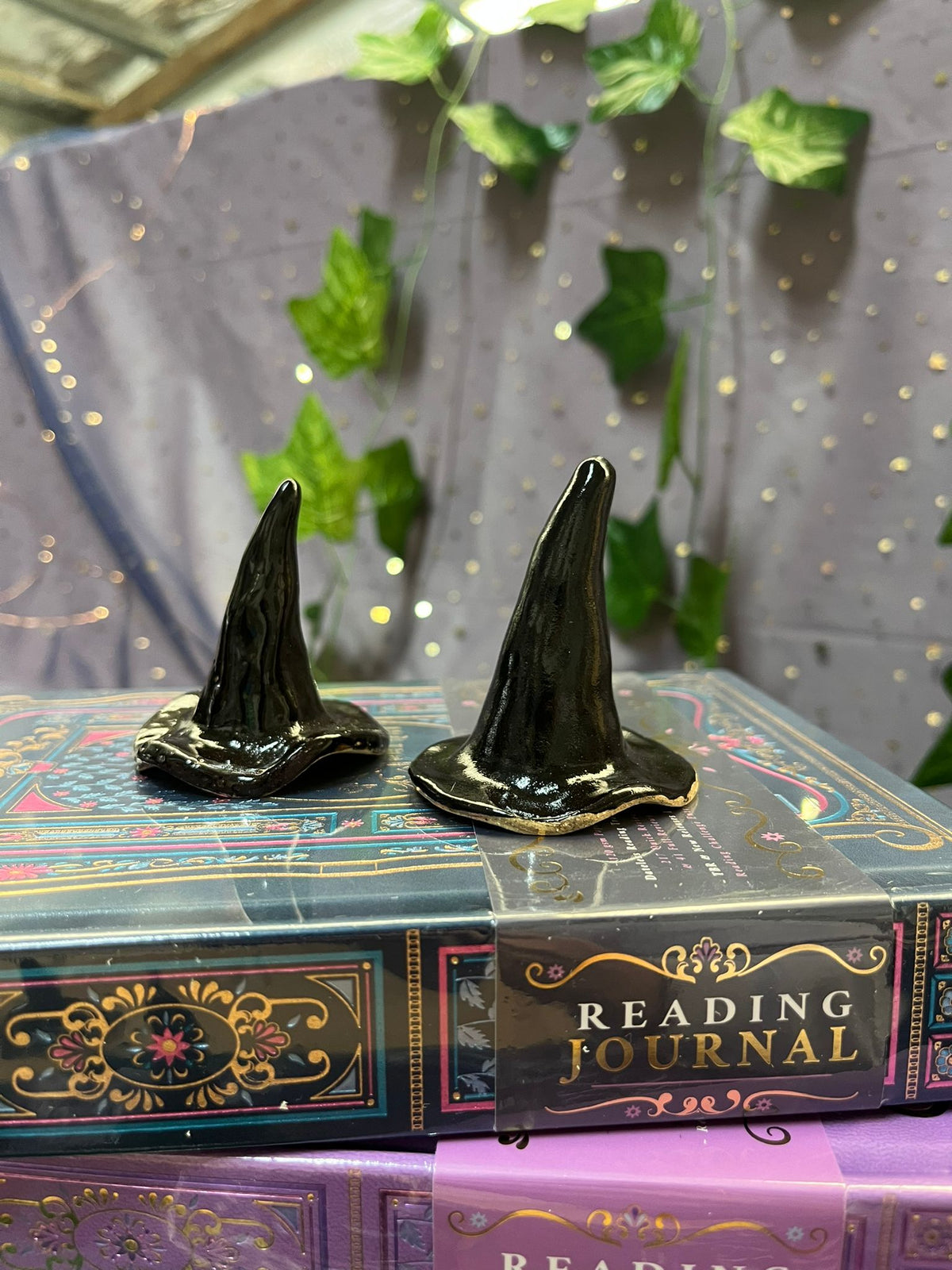 Two black witch hats on top of a book titled 'Reading Journal' with a purple cover.
