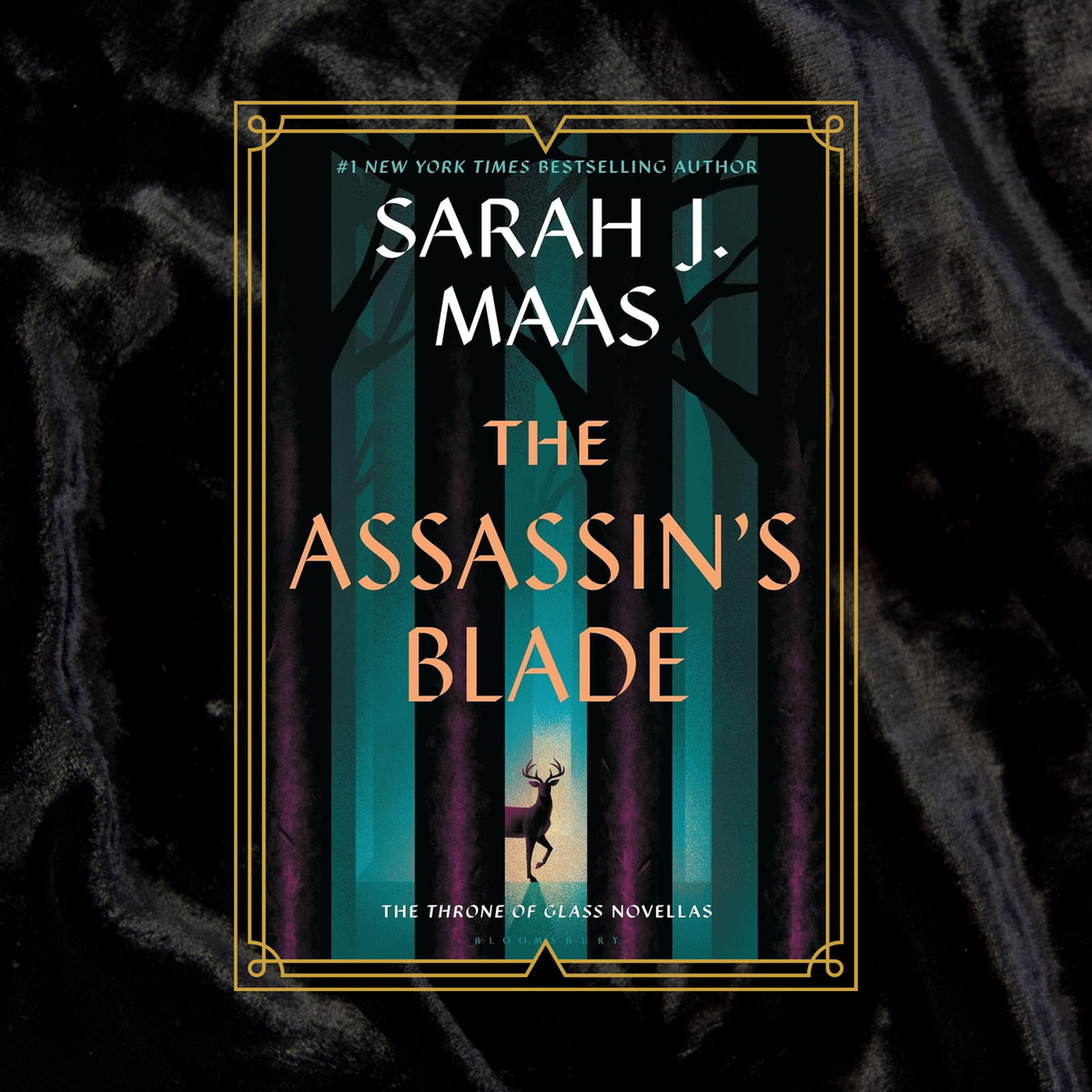 The Assassins Blade by Sarah J Maas book cover with a deer in a forest illustrstion, on a black velvet background.