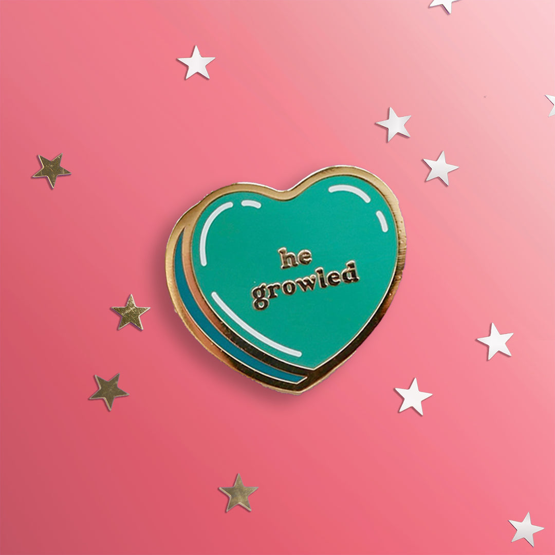 Green heart pin with gold outline: he growled. Shown on a pink background with stars.
